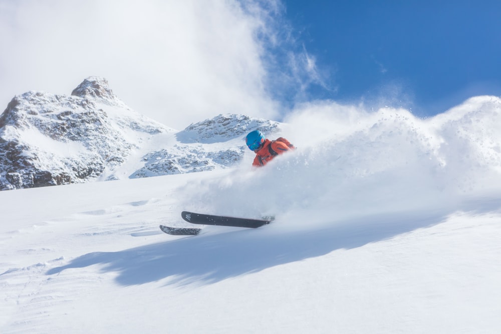 persona in giacca rossa e pantaloni neri che cavalca su snowboard nero su montagna coperta di neve durante