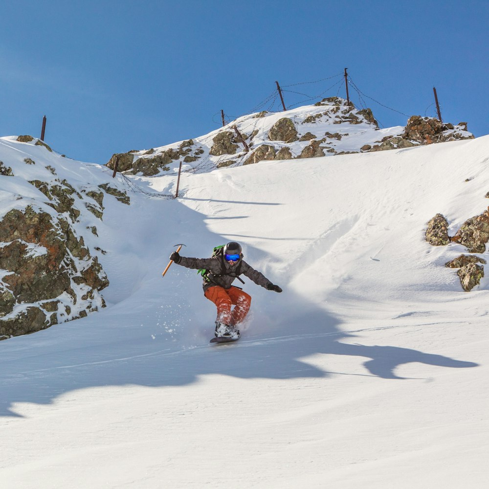 man in red jacket and black pants riding on snowboard on snow covered mountain during daytime