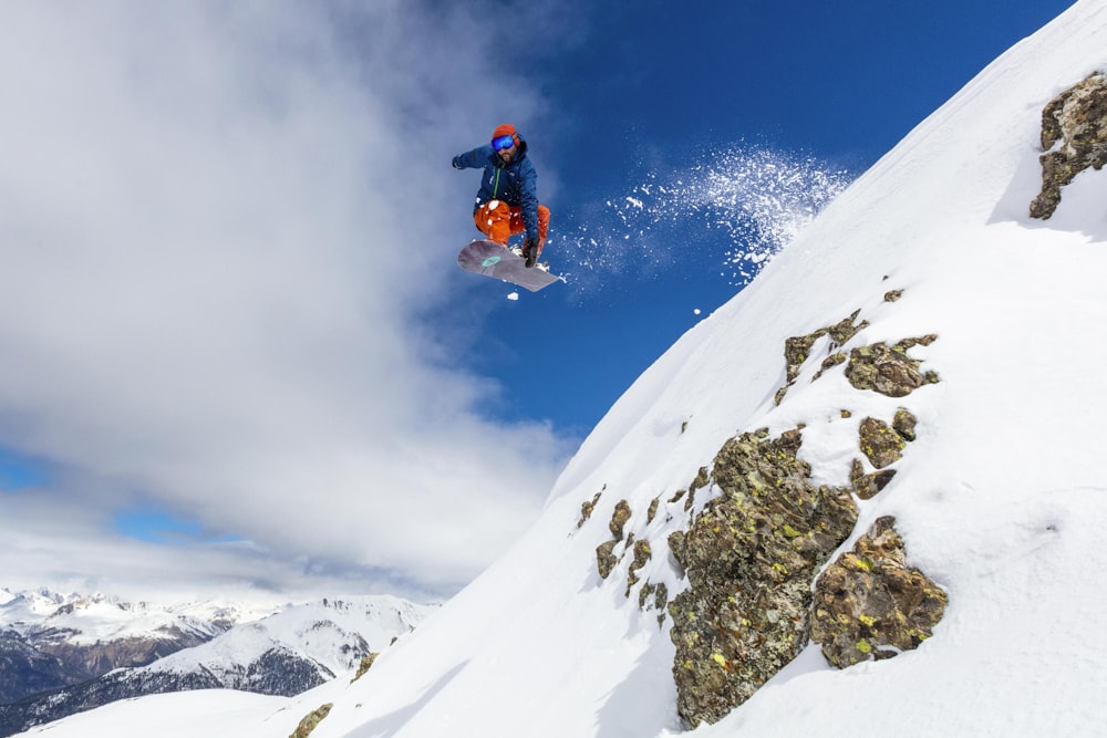 man in red jacket and blue pants sitting on snow covered mountain during daytime