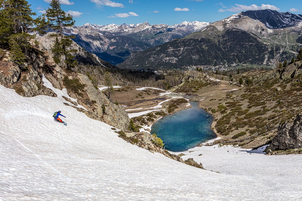 person in red jacket and blue pants sitting on snow covered ground during daytime