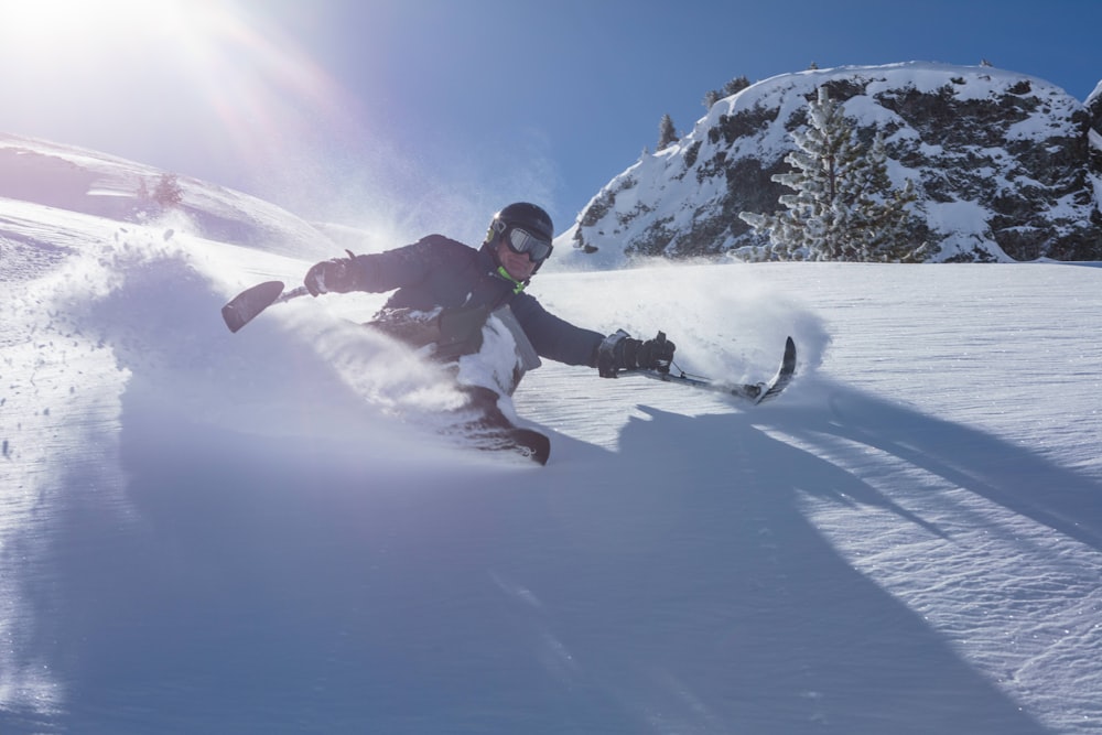 Hombre con chaqueta negra y pantalones blancos haciendo esquí en la nieve durante el día