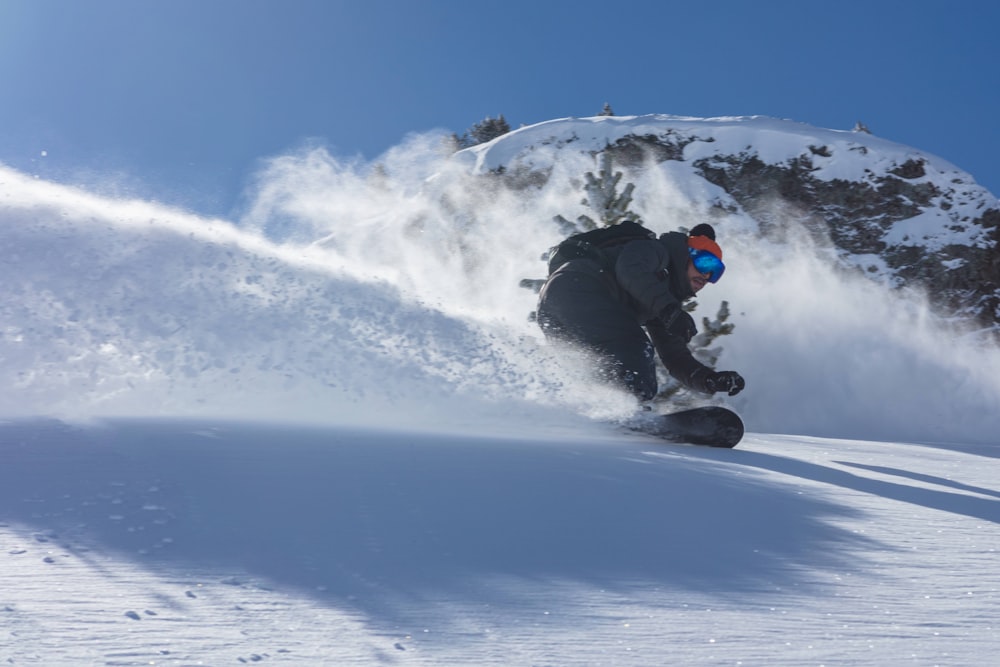 man in black jacket and black pants riding snowboard on snow covered ground during daytime