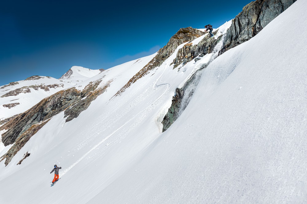pessoa em jaqueta vermelha e calças azuis na montanha coberta de neve durante o dia