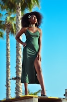 A model stands confidently, adorned in a flowing dress with bold African patterns under warm sunlight.