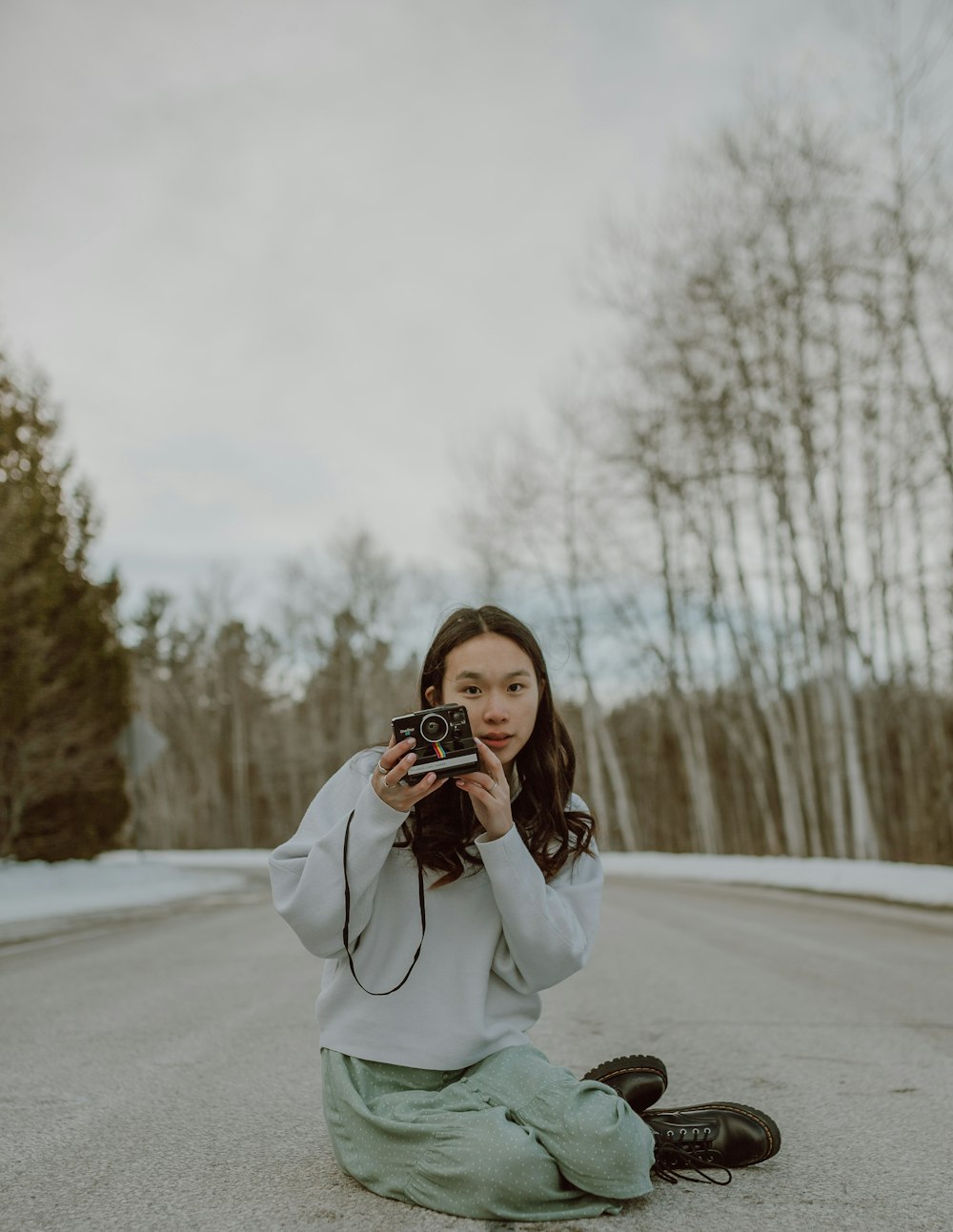 woman in gray coat holding camera on snow covered ground during daytime