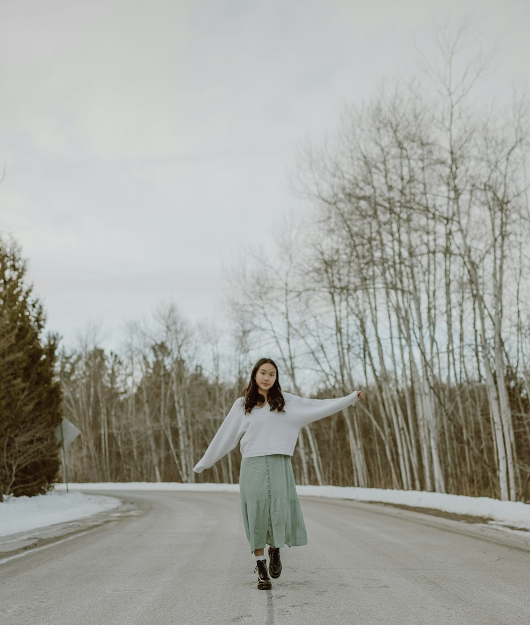 woman in green jacket standing on snow covered road during daytime