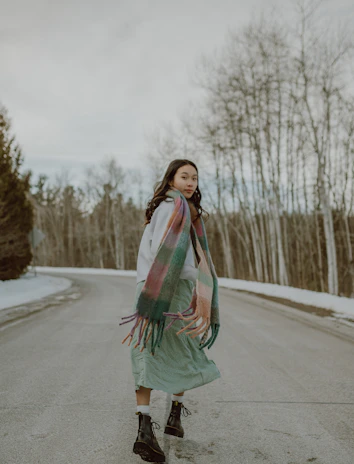 A candid shot of a person walking down a city street wearing a bold patterned scarf and boots.