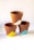 Three terracotta flower pots are stacked in a pyramid formation against a plain white background. Each pot is partially painted with a triangular pattern in different colors: one with white, one with yellow, and one with blue.