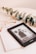 A Kindle device displaying a book titled 'Bridgerton: The Duke & I' rests on top of a closed book titled 'Five Min'. Beside the Kindle, there is a pair of eyeglasses with a gold frame and a sprig of eucalyptus leaves, all placed on a pale beige surface.
