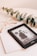 A Kindle device displaying a book titled 'Bridgerton: The Duke & I' rests on top of a closed book titled 'Five Min'. Beside the Kindle, there is a pair of eyeglasses with a gold frame and a sprig of eucalyptus leaves, all placed on a pale beige surface.
