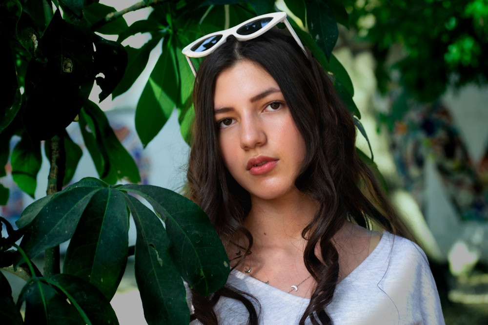 a woman wearing sunglasses standing next to a tree