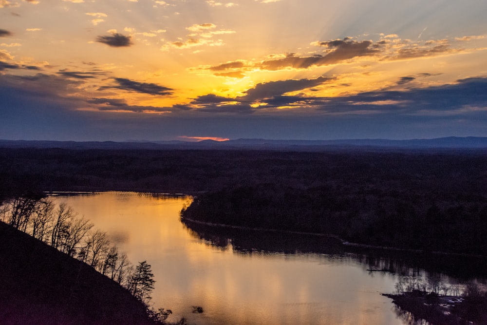 body of water near trees during sunset