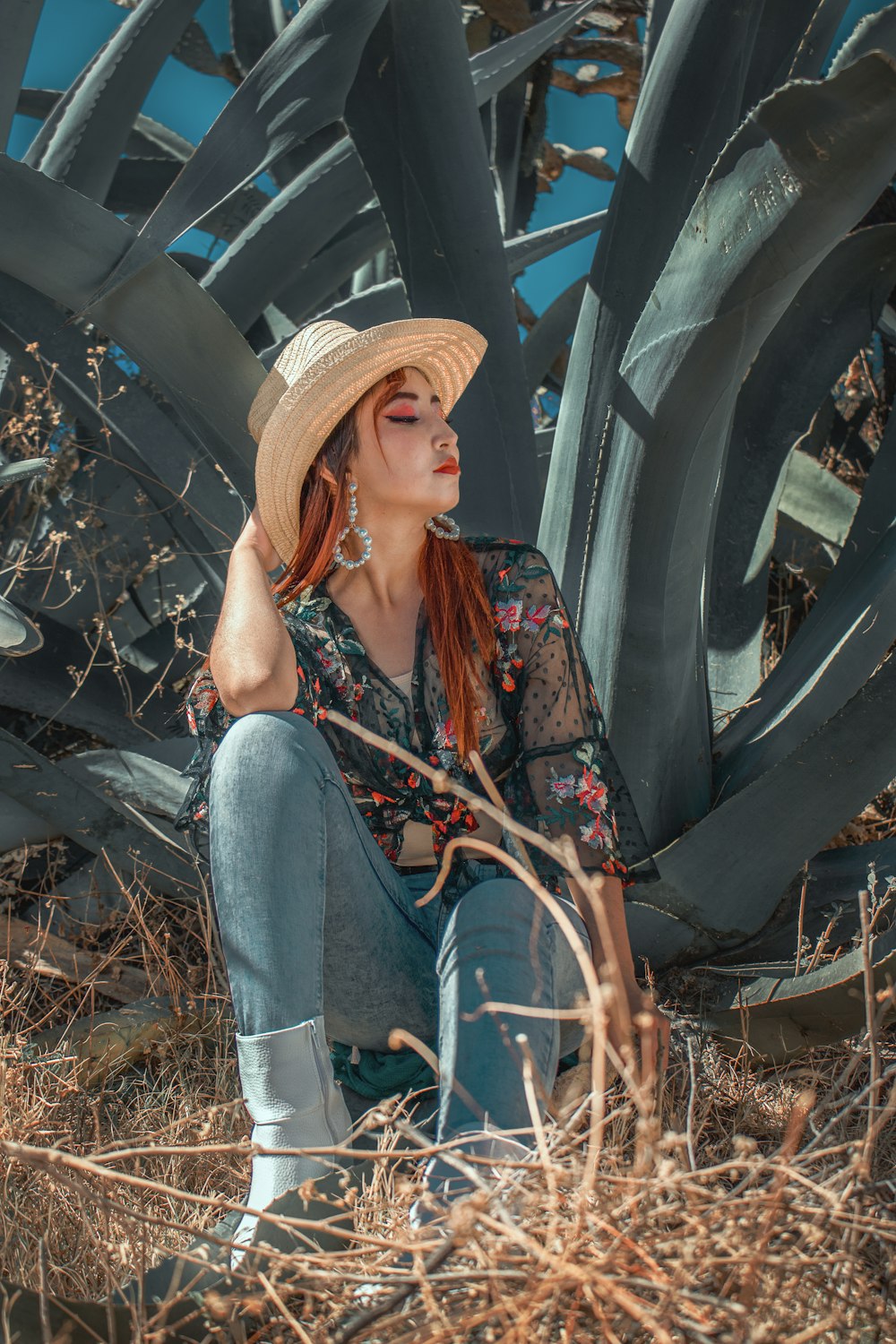 woman in blue denim jeans and brown hat sitting on brown dried leaves