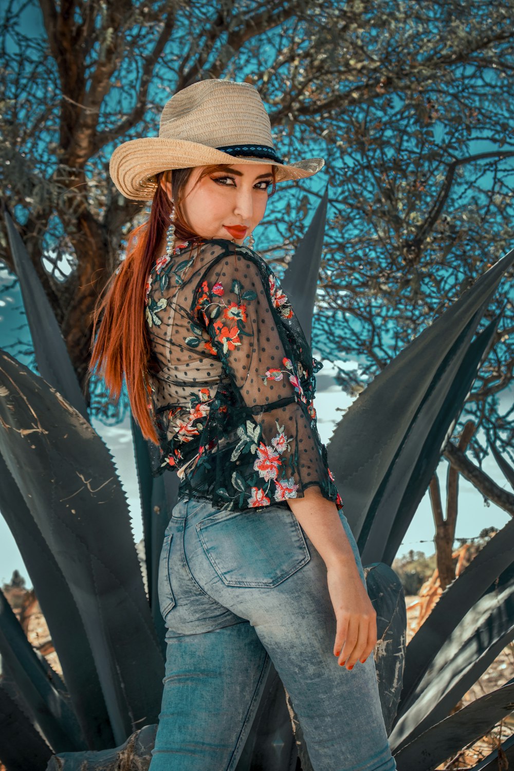 woman in blue denim jeans and brown hat standing beside black tree during daytime