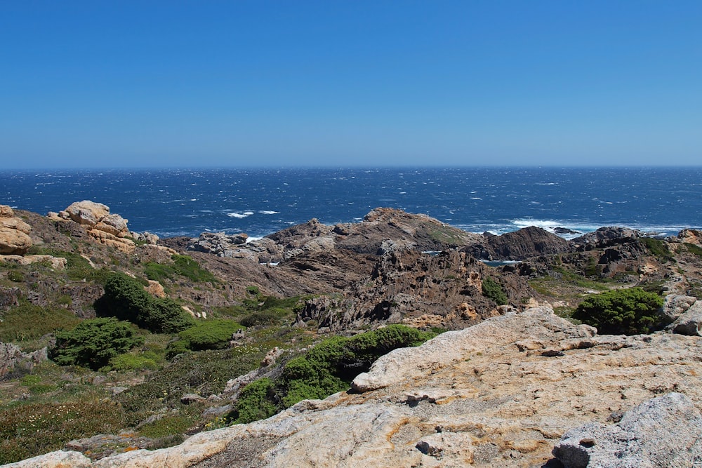 green and brown mountain beside blue sea under blue sky during daytime