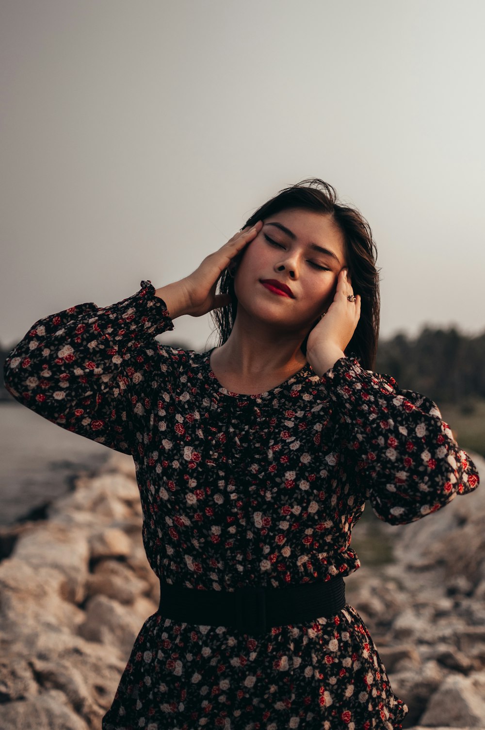 woman in black and red floral long sleeve shirt standing on brown rock during daytime