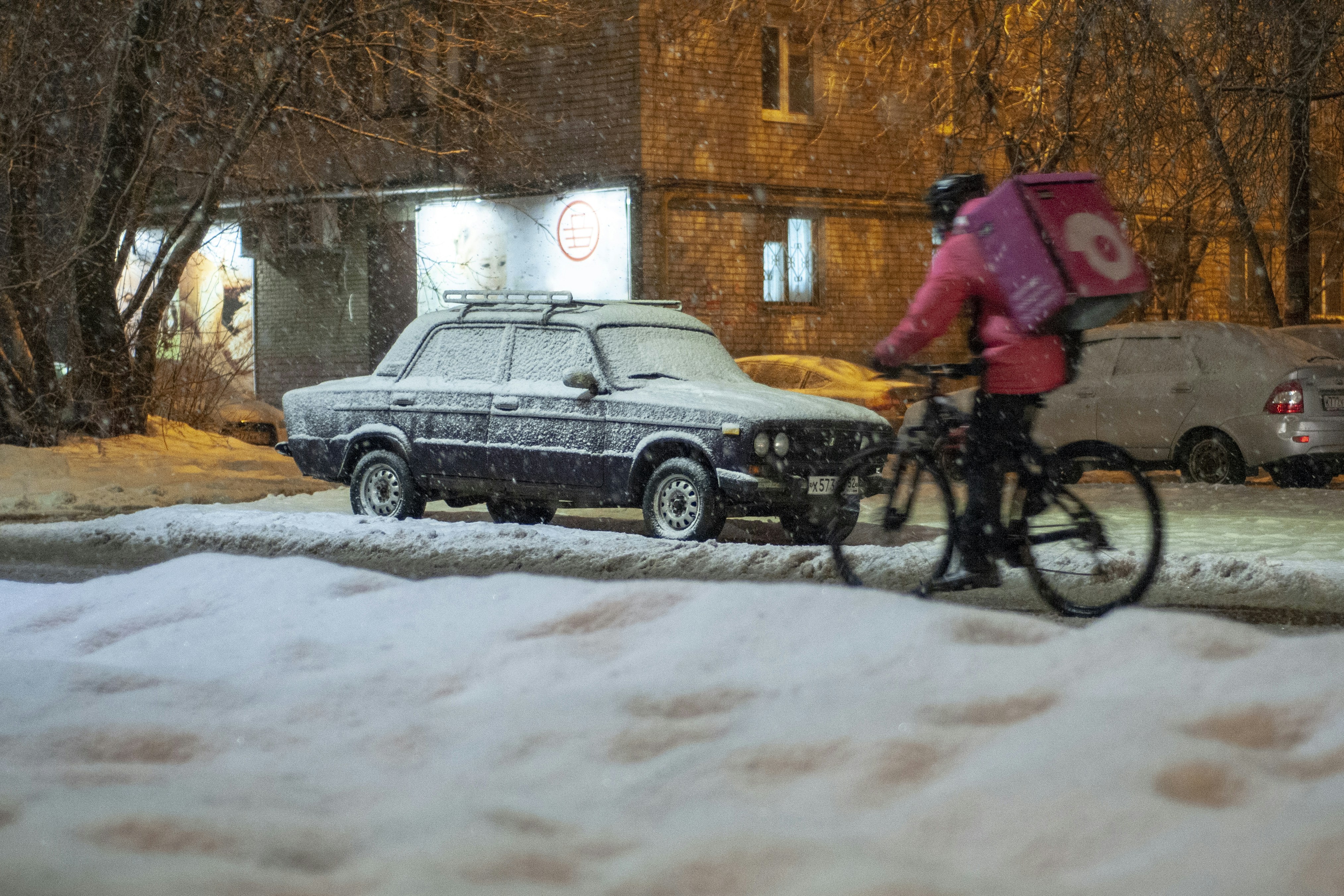 A courier carries an order on a bicycle during a snowfall