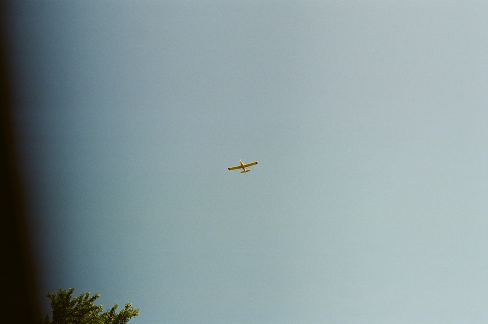 yellow plane flying over green trees during daytime