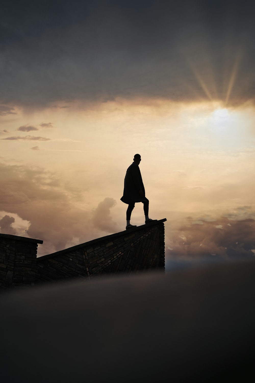 silhouette of man standing on concrete wall during sunset