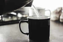 Close-up of a hand pouring hot water from a shiny electric kettle into a mug.