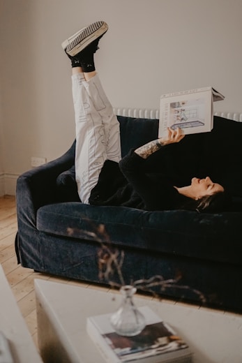 man in white pants lying on black couch