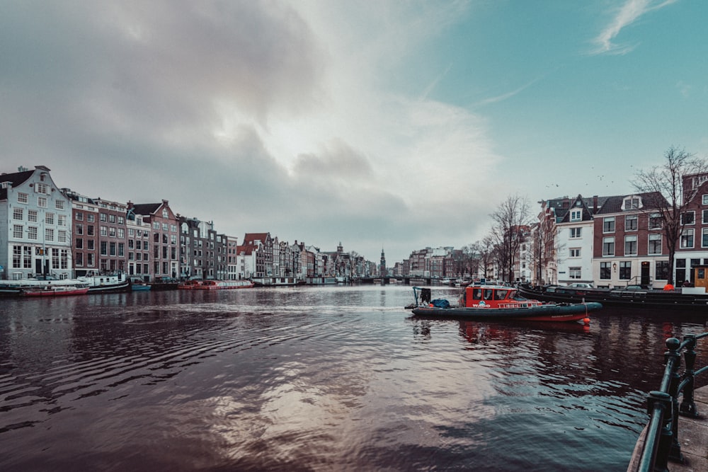 red boat on body of water near city buildings during daytime