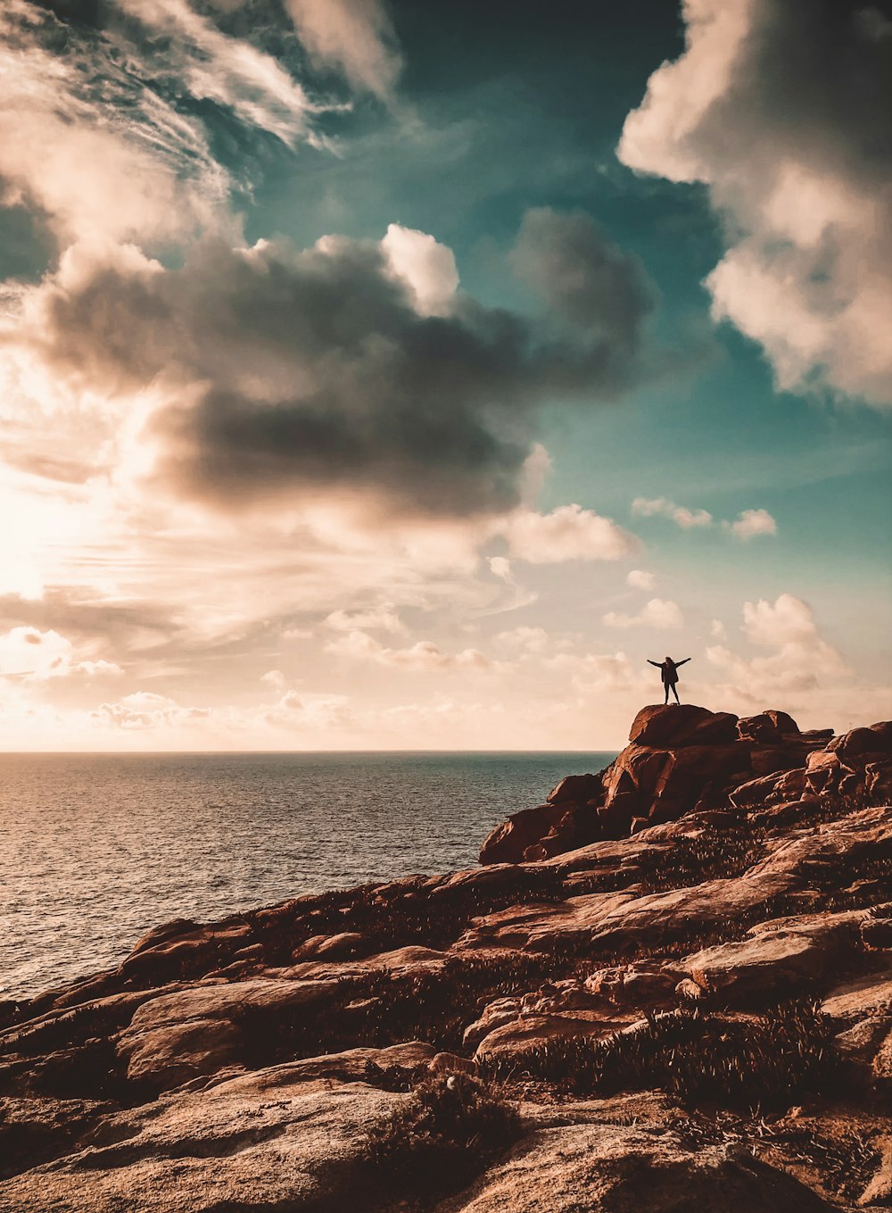 person standing on brown rock formation near body of water during daytime