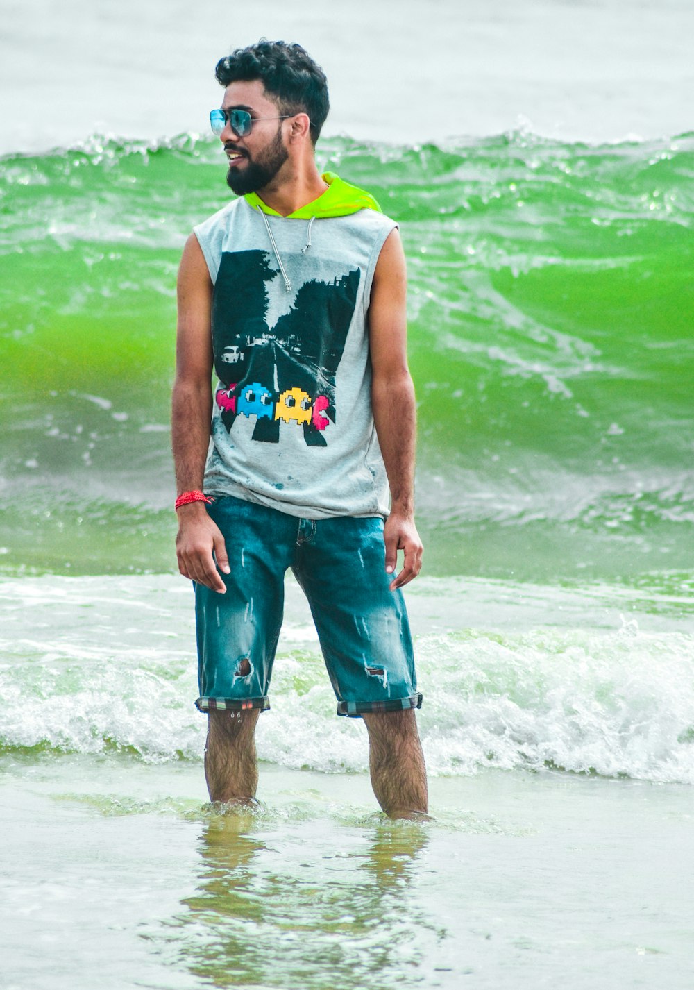 Uomo in canottiera verde e pantaloncini blu in piedi sulla riva del mare durante il giorno