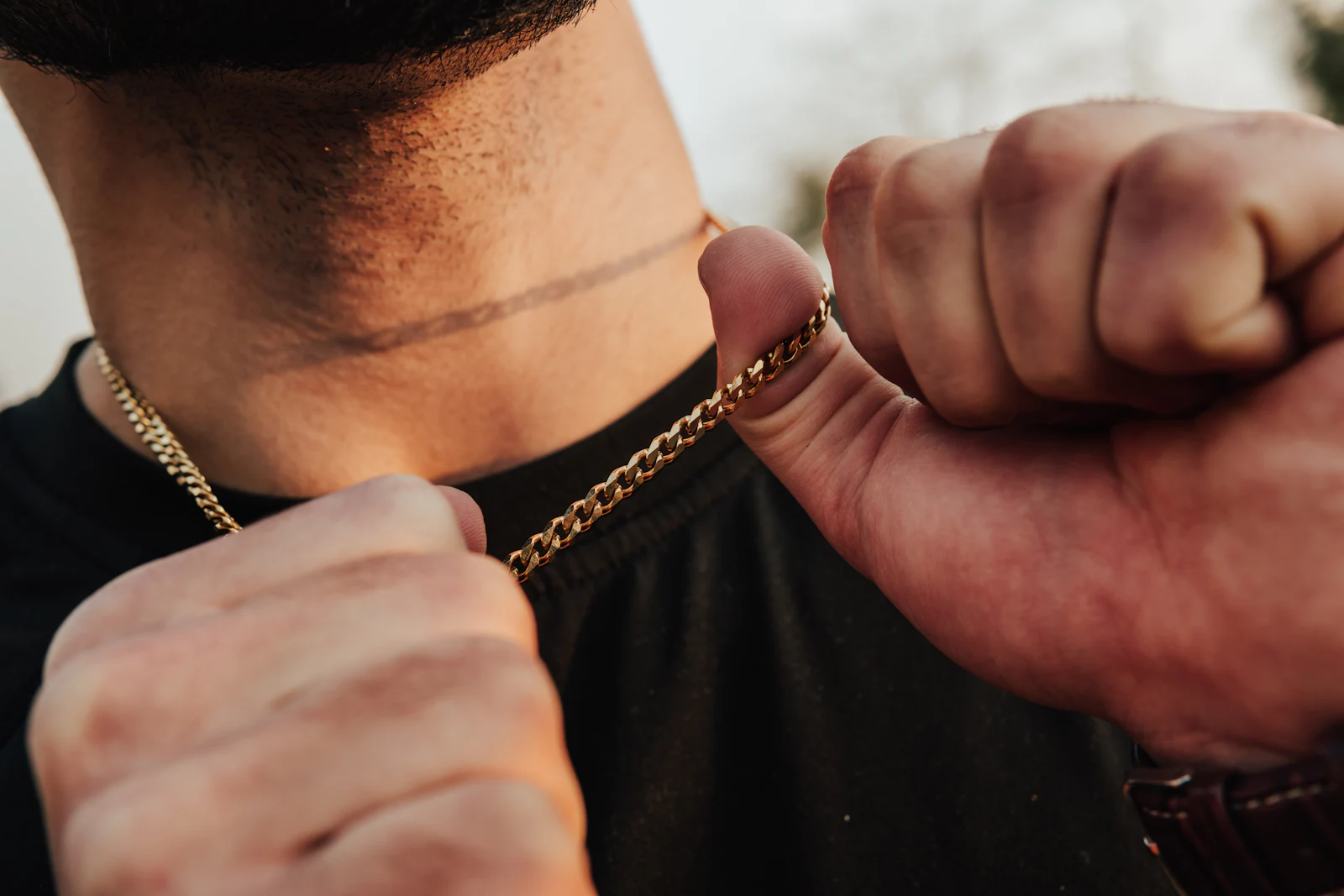 Two hands pulling a collar open to show a heavy yellow gold curb chain.
