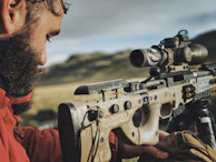 Close-up of a shooter adjusting their sights on a precision rifle at an indoor range.