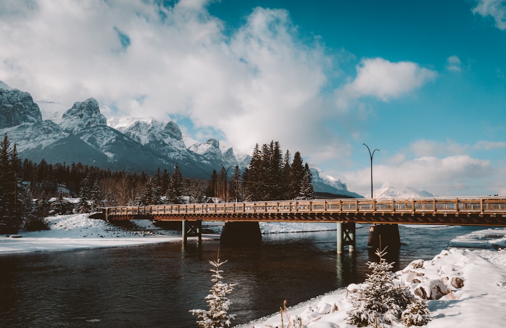 ponte di legno marrone sul fiume vicino alla montagna coperta di neve durante il giorno