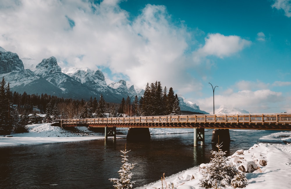 Braune Holzbrücke über den Fluss in der Nähe des schneebedeckten Berges tagsüber