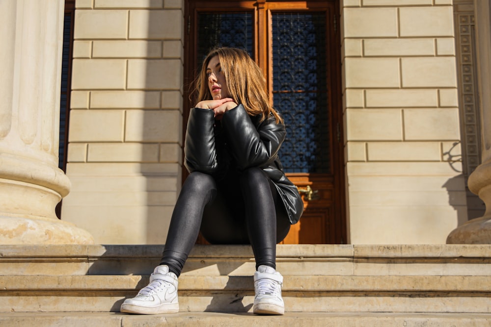 woman in black leather jacket and black pants sitting on brown wooden window