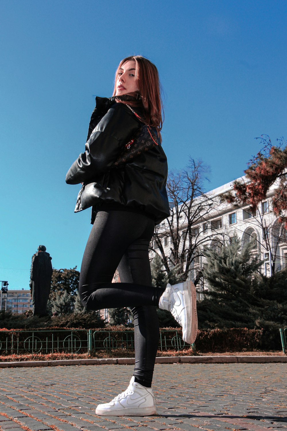 woman in black leather jacket and black pants sitting on brown wooden fence during daytime