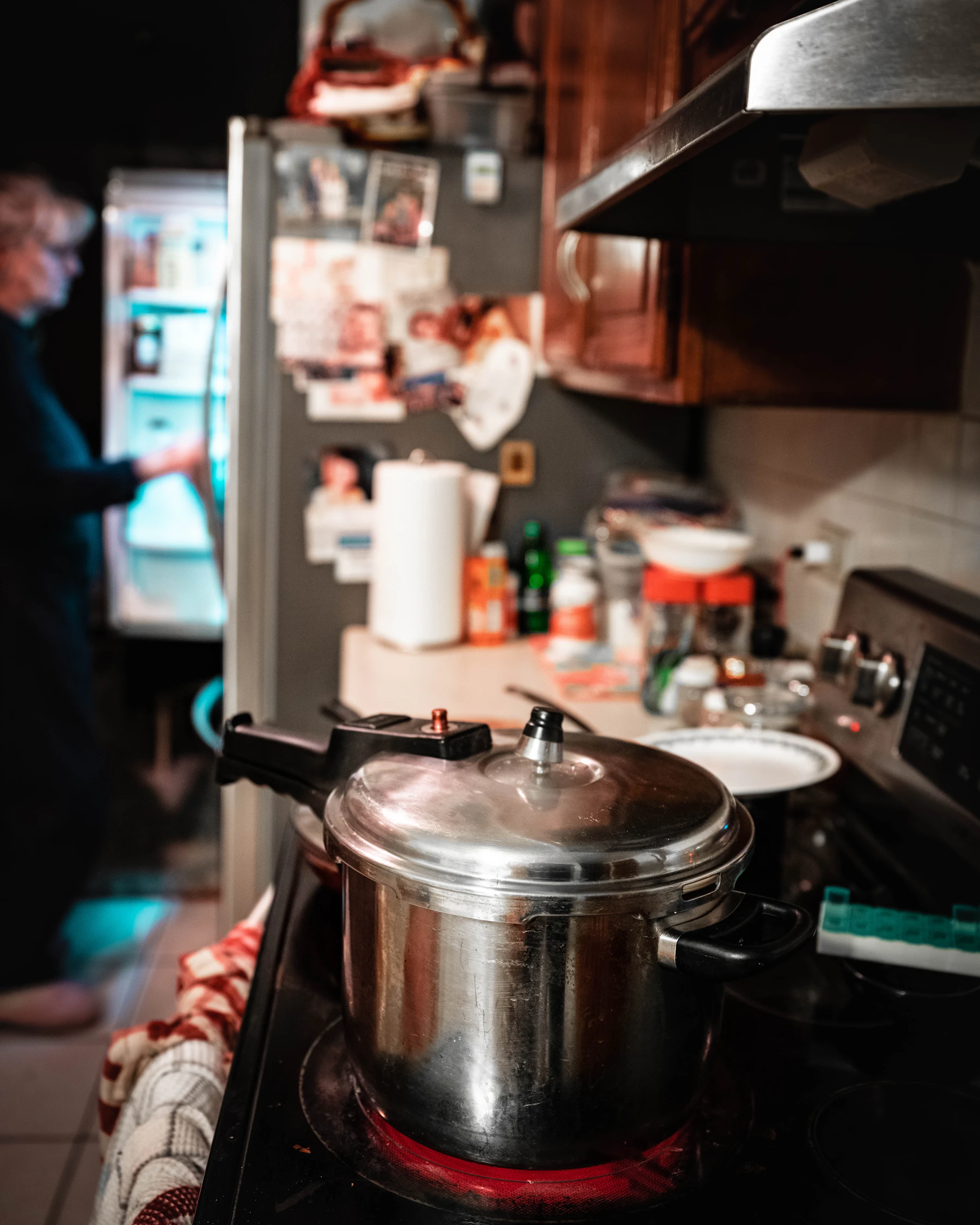 A stainless stovetop pressure cooker on a glowing electric burner in a home kitchen at night