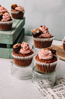Hand-decorated cupcakes with soft pink frosting and tiny edible pearls arranged on a wooden stand