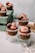 Cupcakes topped with pink frosting and garnished with nuts and chocolate, displayed on glass surfaces. They are arranged creatively with some cupcakes elevated on clear glass cups and others placed on a wooden crate.