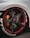 A close-up view of a customized car wheel featuring a carbon fiber rim with red accents. The tire has prominent white lettering and the brake caliper is in a contrasting orange shade.