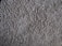 A close-up view of a textured, plush carpet with dense, fibrous strands in a neutral beige color.