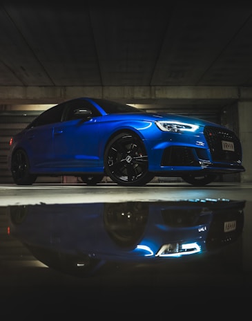 Front view of a polished electric blue sports coupe reflecting city lights.