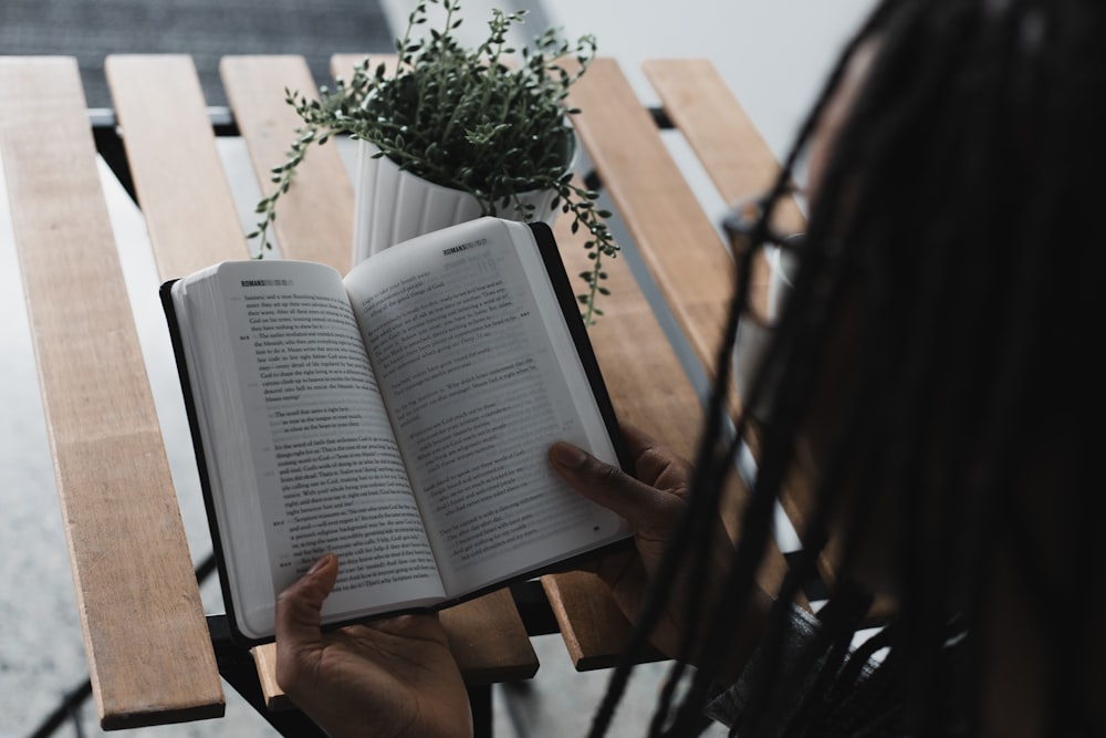 person reading book on brown wooden bench