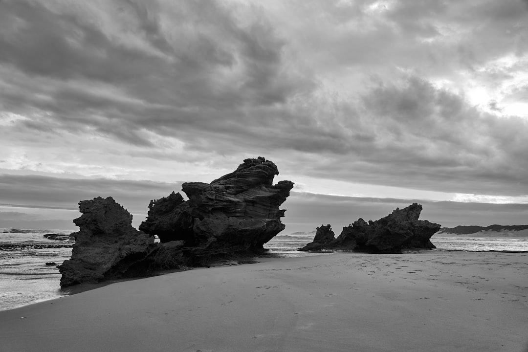 grayscale photo of rock formation on sea shore
