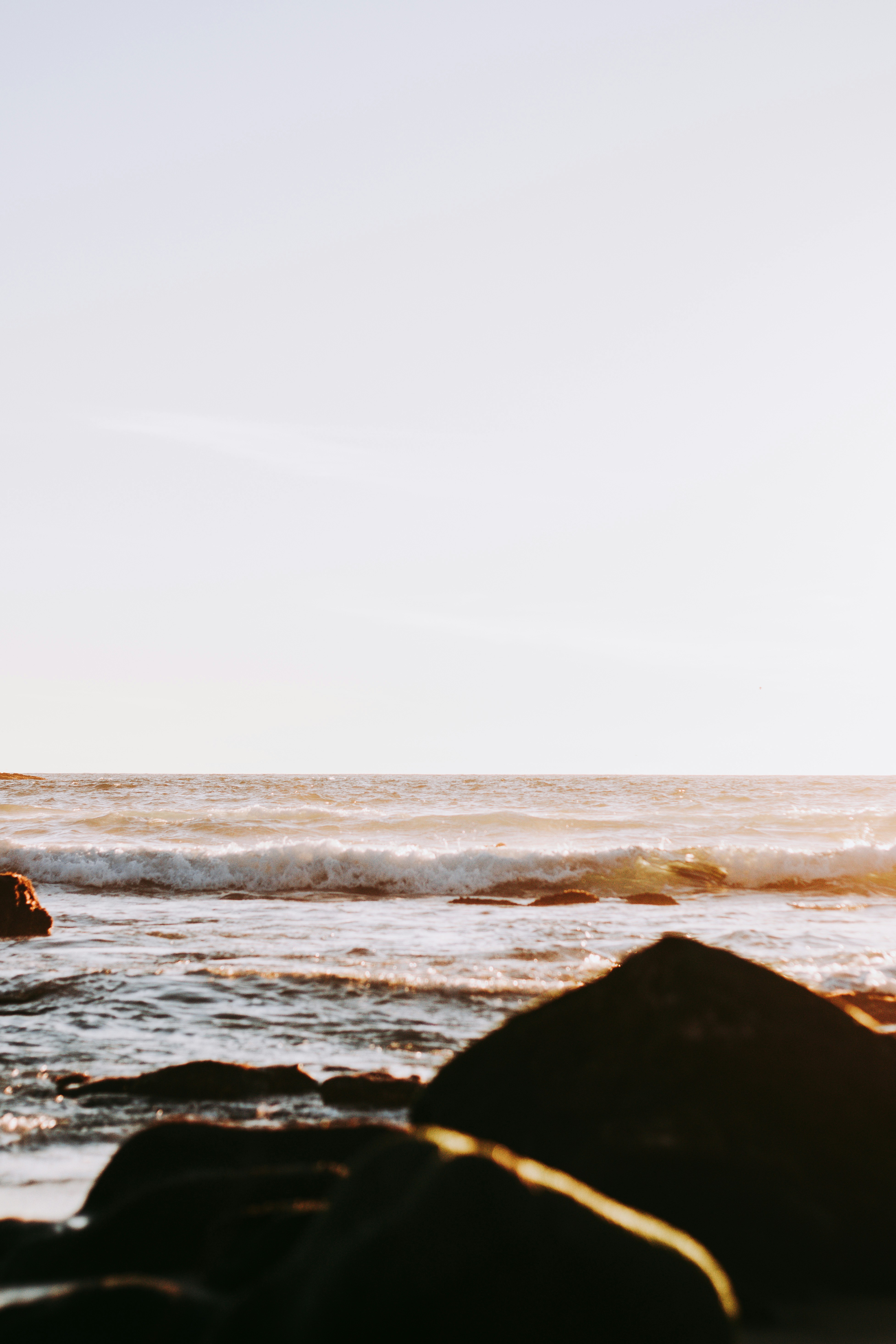 Person in schwarzen Shorts, die tagsüber auf einem Felsen in der Nähe des Meeres sitzt