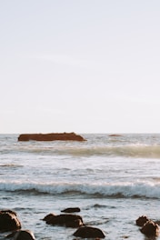 Serene coastal scene with waves gently lapping against rocks under a soft sunrise.