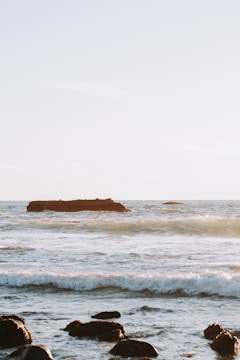 Serene coastal scene with waves gently lapping against rocks under a soft sunrise.