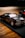 A detailed miniature model car with a sleek design and custom flame decals on the sides, featuring a prominent engine that sticks out of the hood. The car sits on a black mat, which contrasts with the wooden surface beneath.