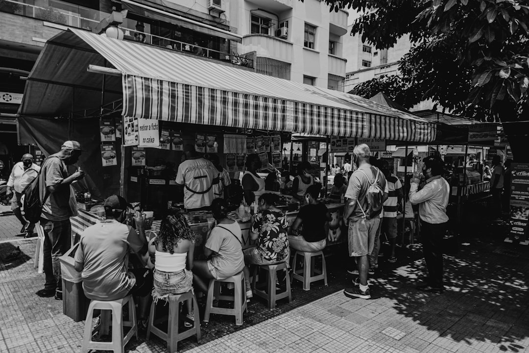 grayscale photo of people sitting on chairs near building