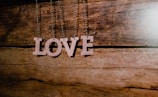 Wooden letters forming the word 'LOVE' hang from strings against a rustic wooden background.