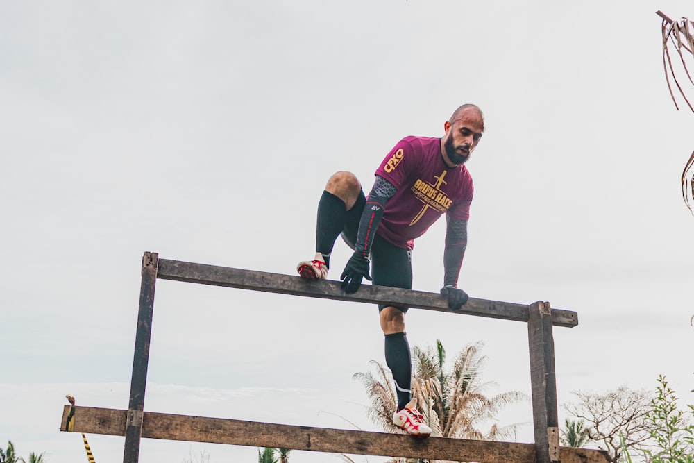 man in red and black crew neck t-shirt standing on brown wooden fence during daytime