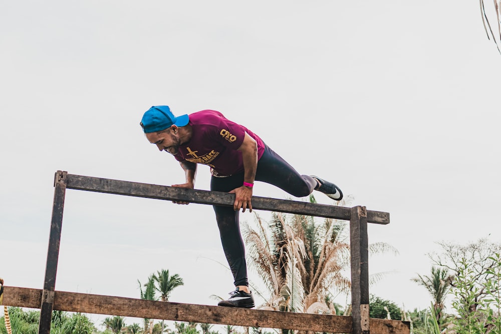 woman in purple long sleeve shirt and blue fitted cap climbing on brown wooden fence during